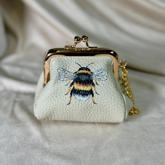 Small white purse with bee design on a light fabric background