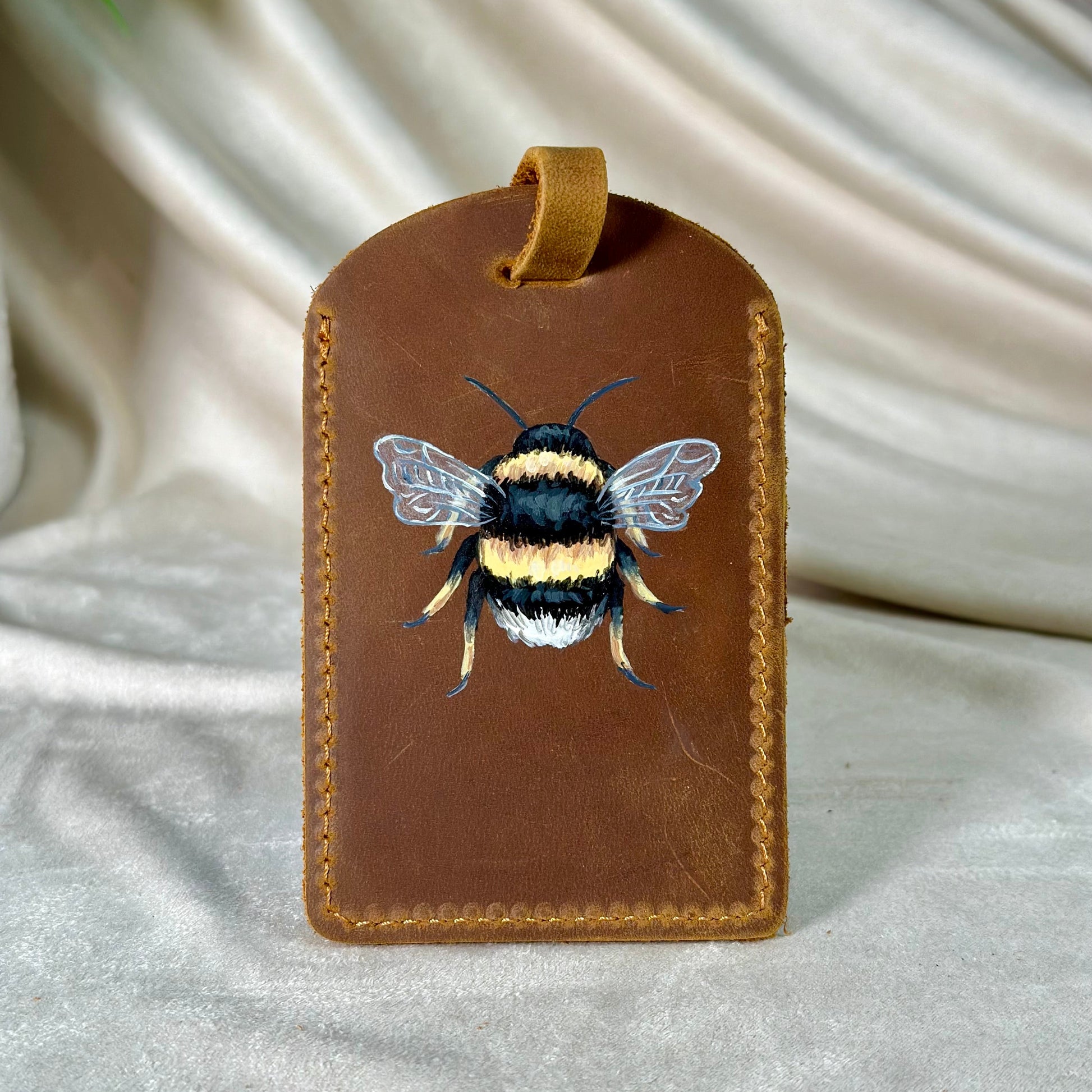 Brown leather tag with a bee illustration on a white fabric background