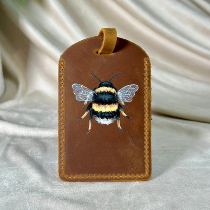 Brown leather tag with a bee illustration on a white fabric background