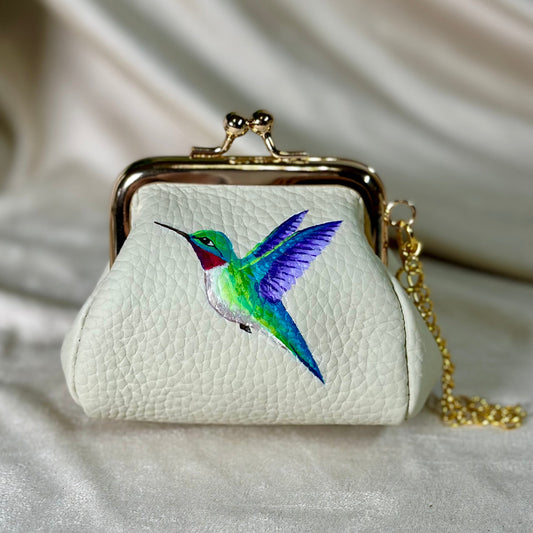 Small white purse with a colorful hummingbird design on a beige fabric background