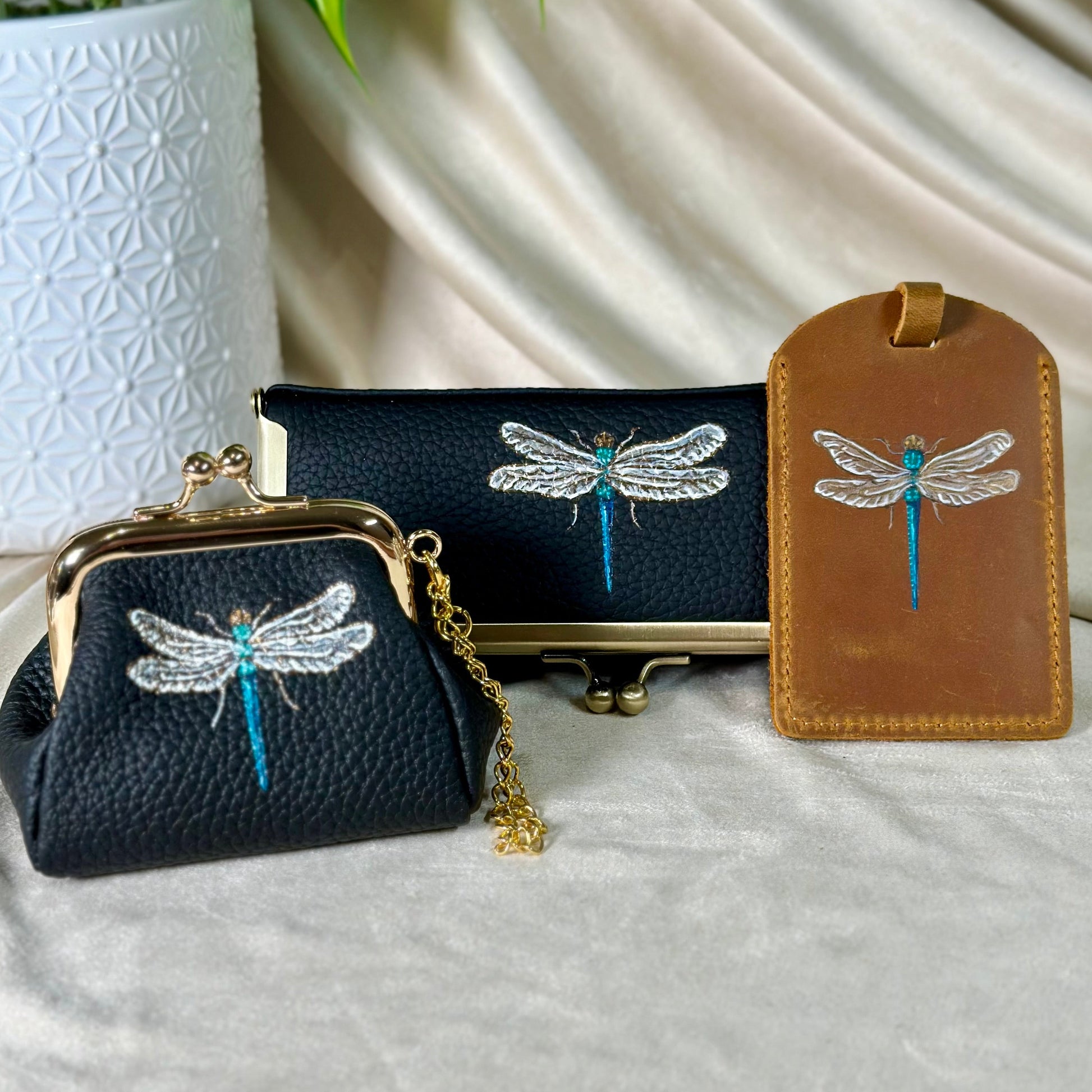 Black clutch with dragonfly design, stand, and brown luggage tag on a light background