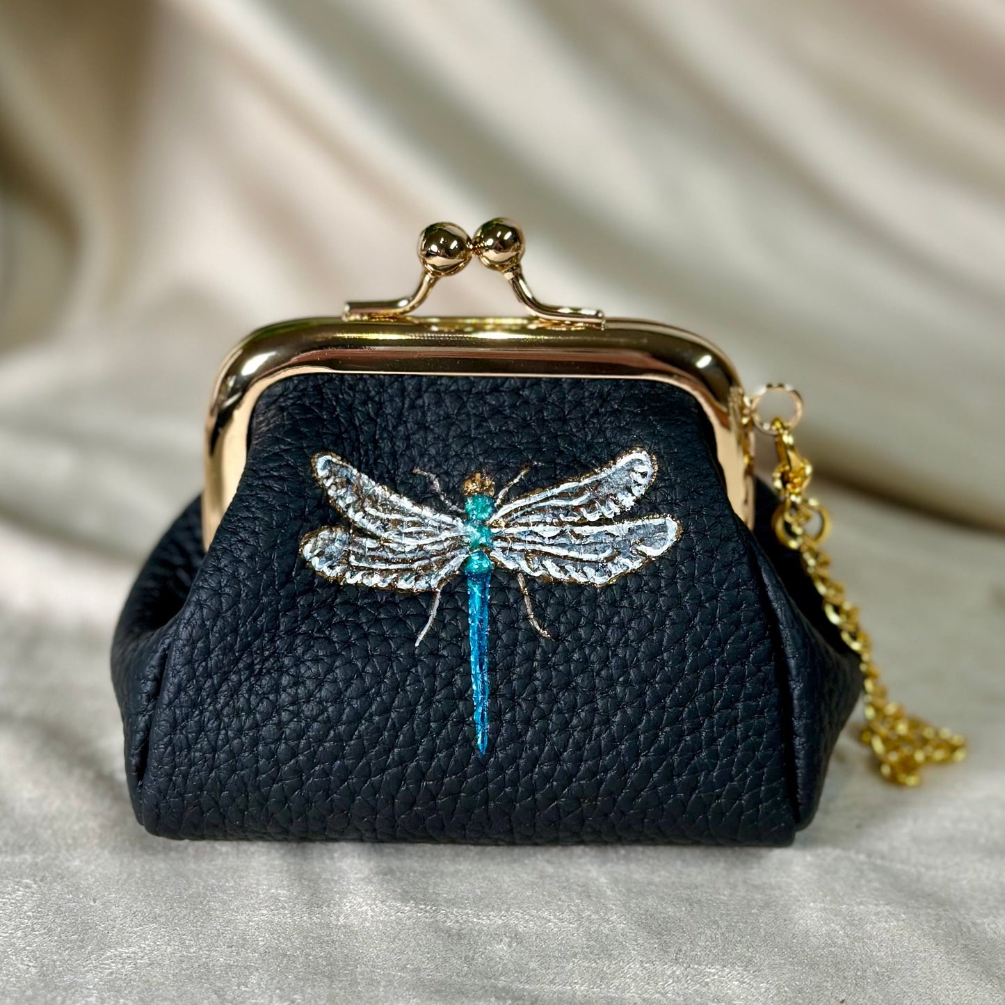 Black purse with dragonfly design on a beige fabric background