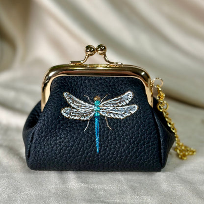 Black purse with dragonfly design on a beige fabric background