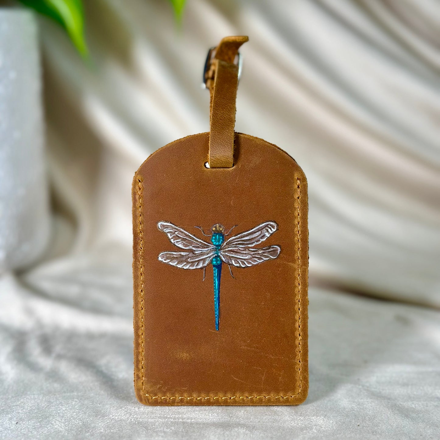 Brown leather luggage tag with dragonfly design on a white fabric background