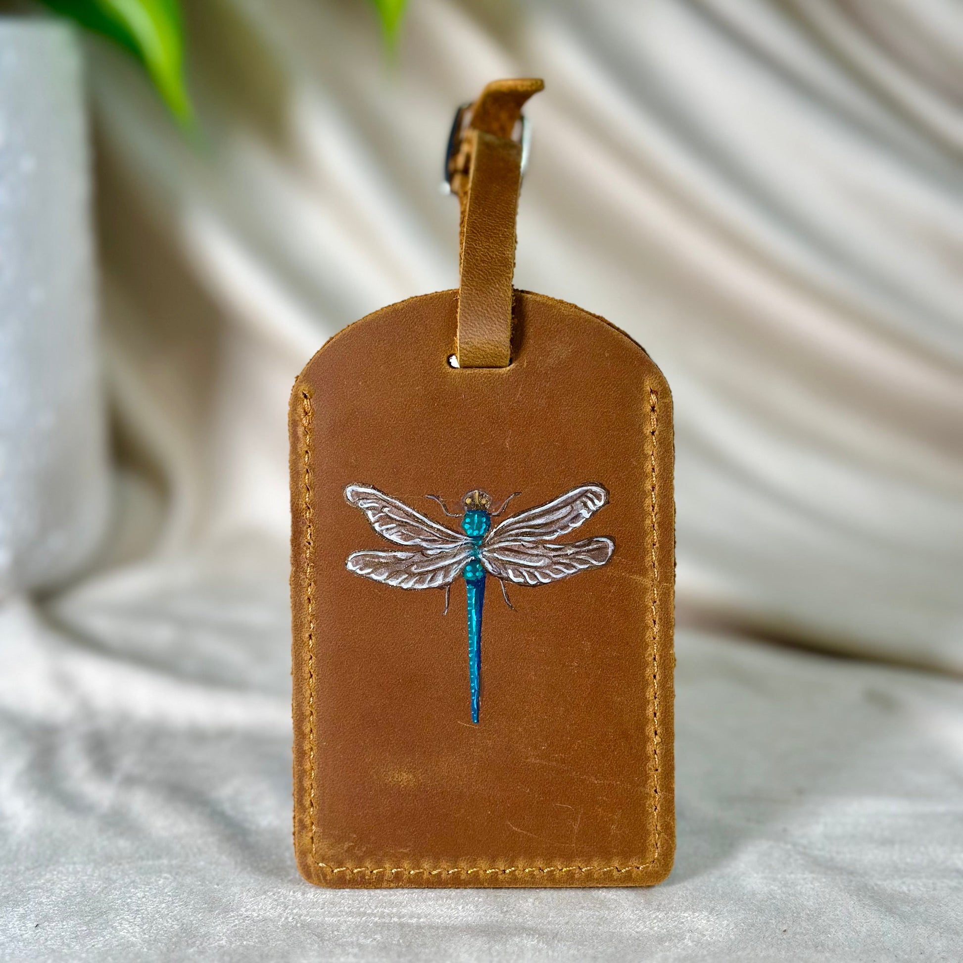 Brown leather luggage tag with dragonfly design on a white fabric background