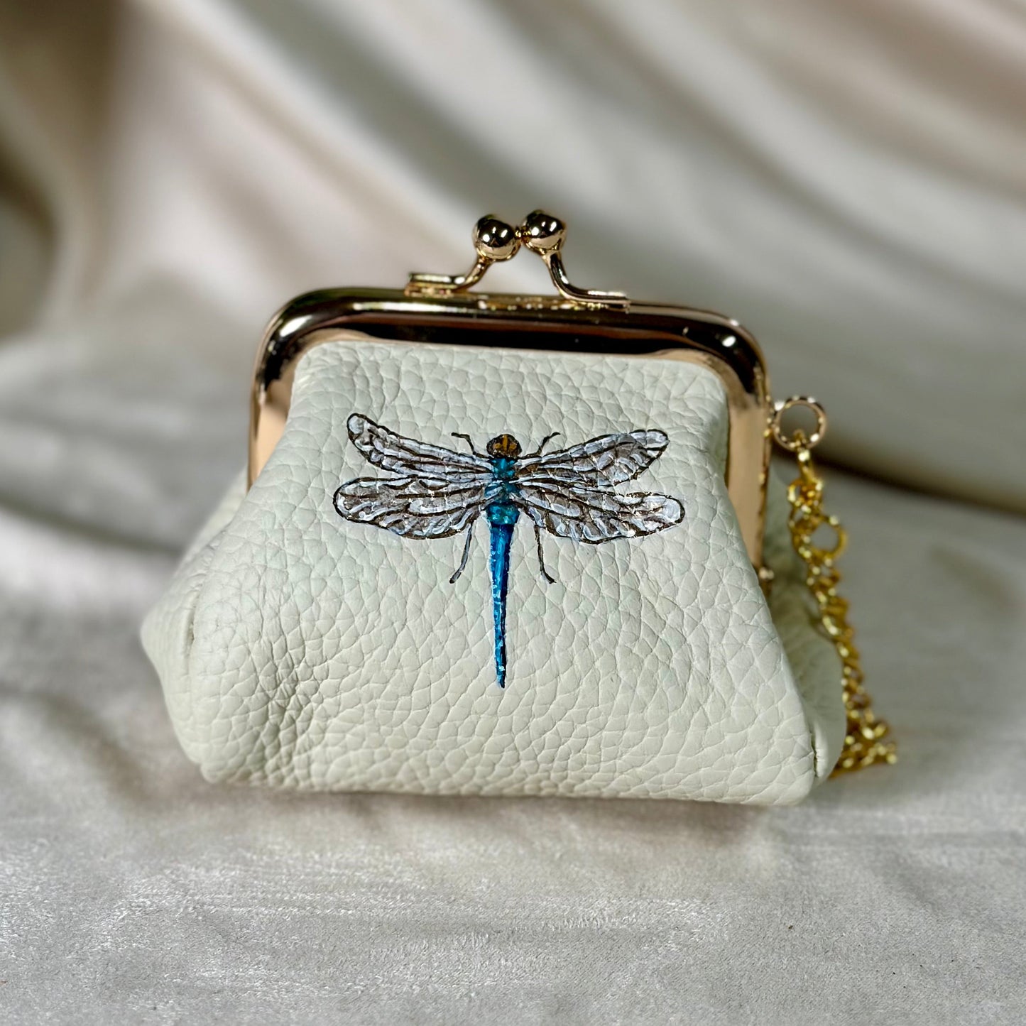 Small white purse with dragonfly design on a light fabric background