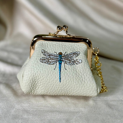 Small white purse with dragonfly design on a light fabric background