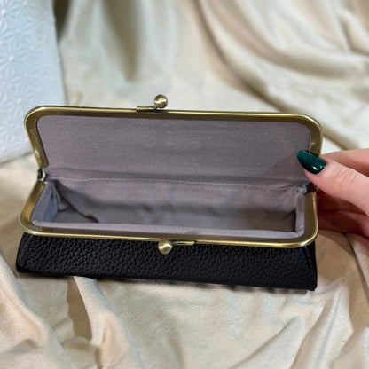 Black clutch with gold clasp held by a hand on a light fabric background