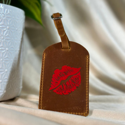 Brown leather luggage tag with red lip print on a neutral background