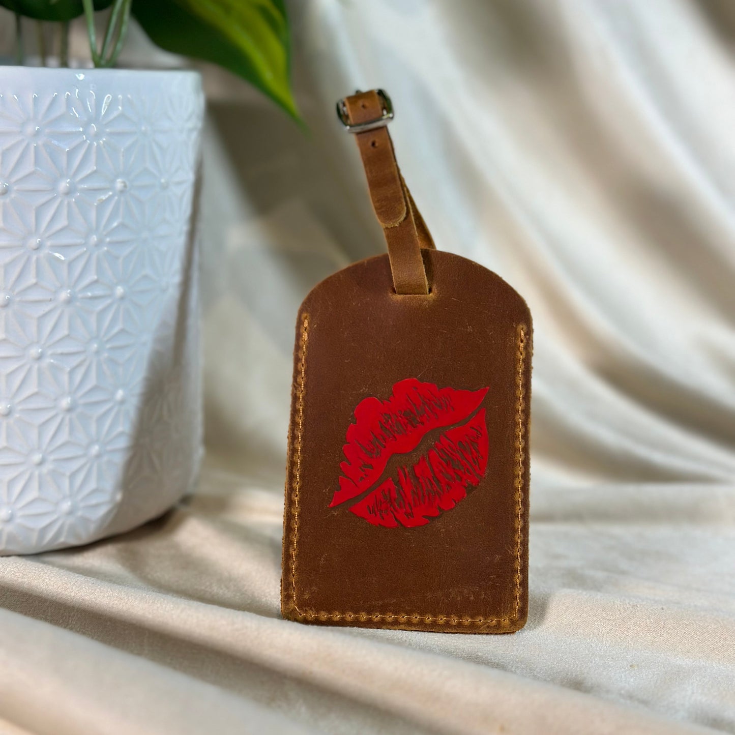 Brown leather luggage tag with red lip print on a light fabric background