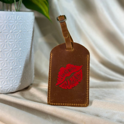 Brown leather luggage tag with red lip print on a light fabric background