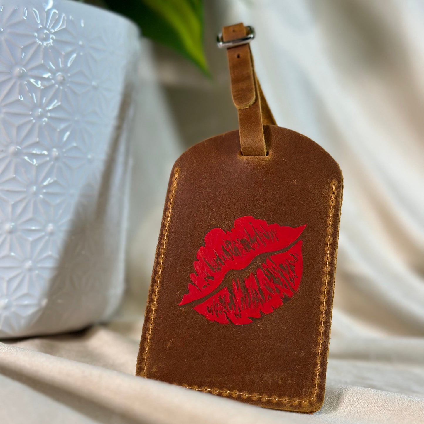 Brown leather luggage tag with red lip print on a neutral background