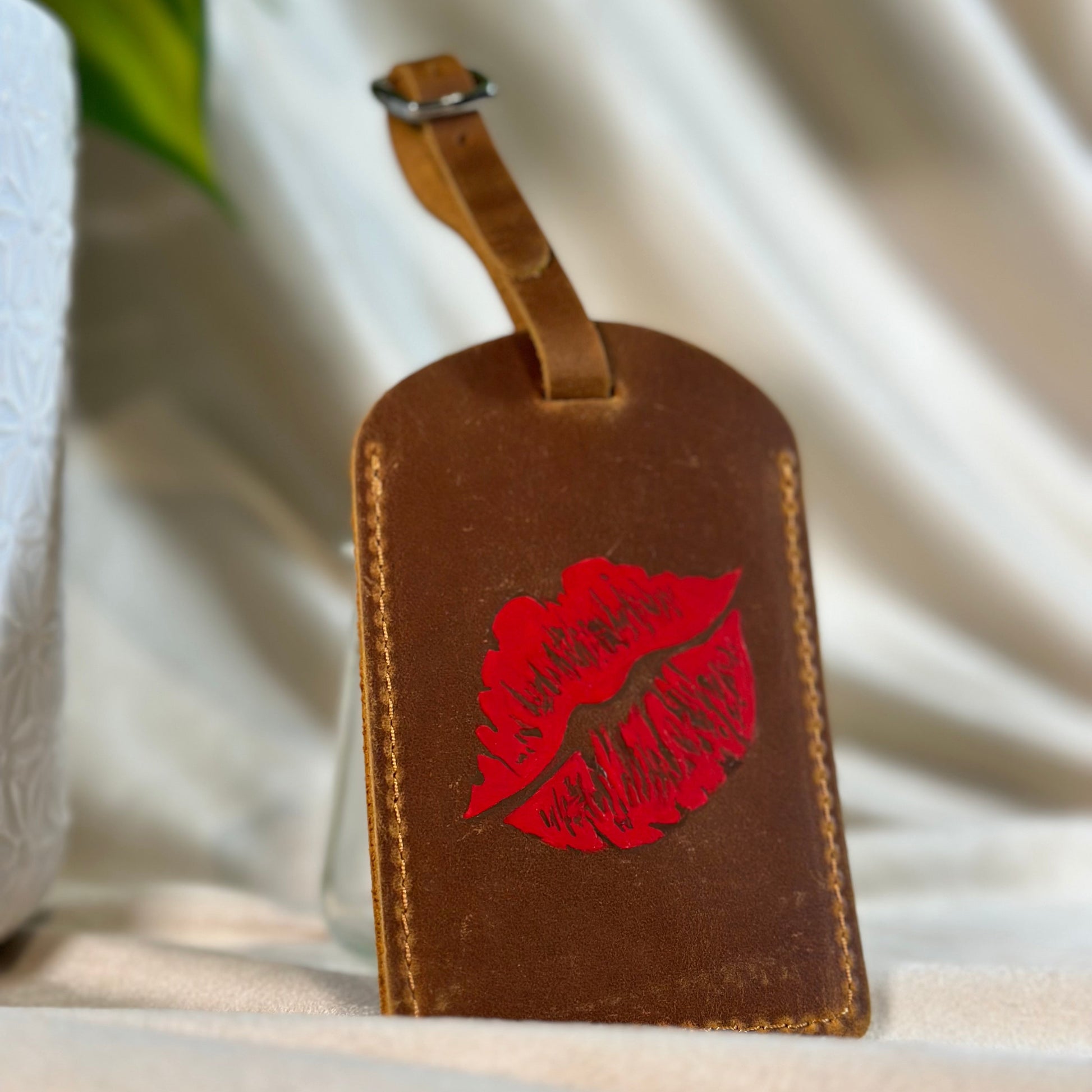 Brown leather luggage tag with red lip print on a light background