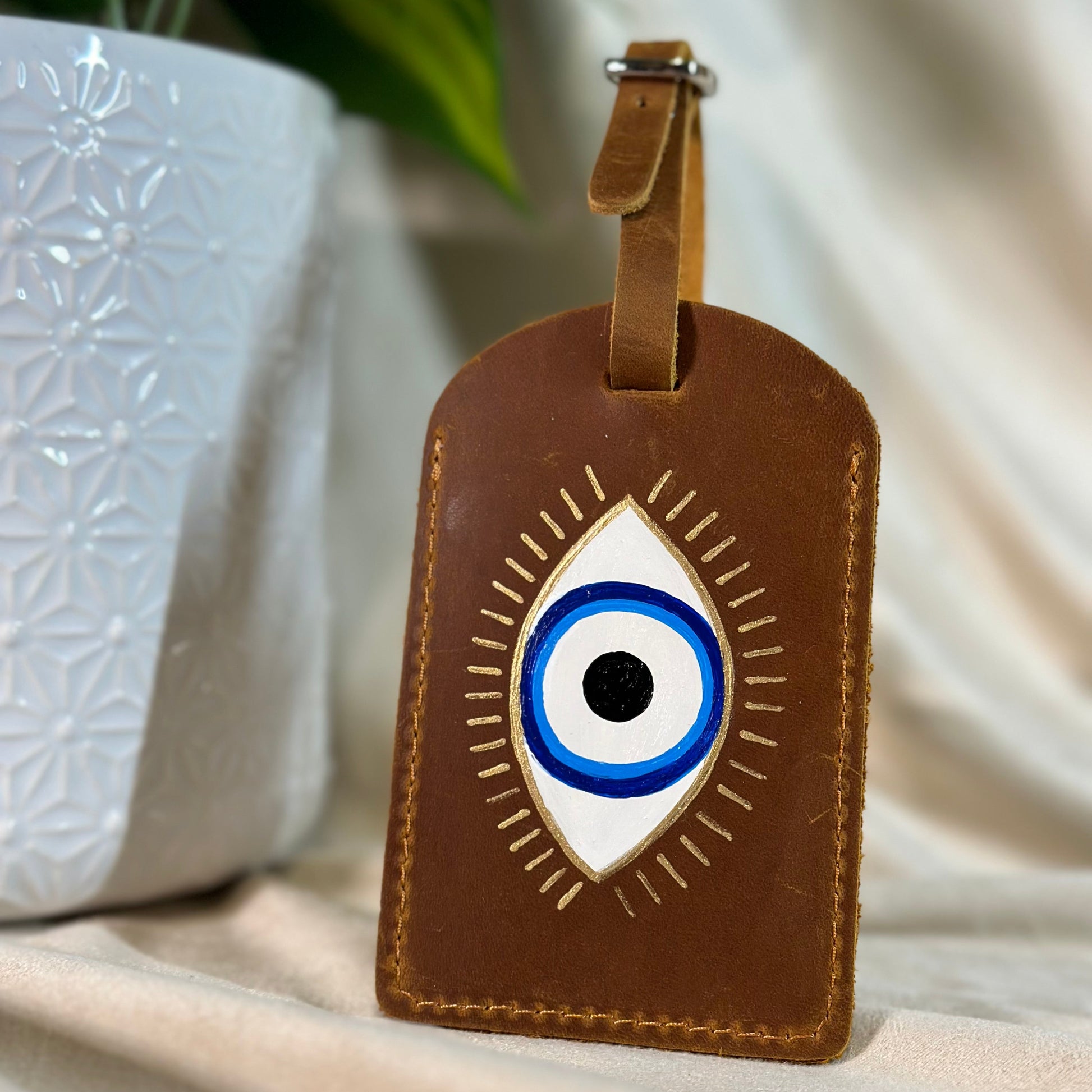 Brown leather luggage tag with eye design on a neutral background