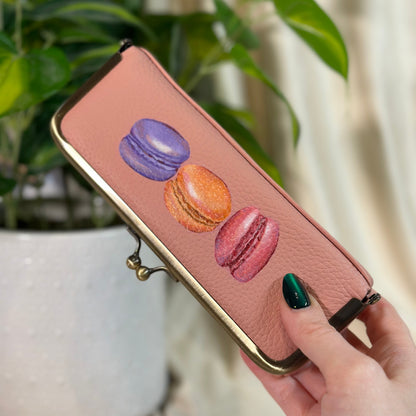 Pink phone case with macaron designs held by a hand against a blurred indoor background
