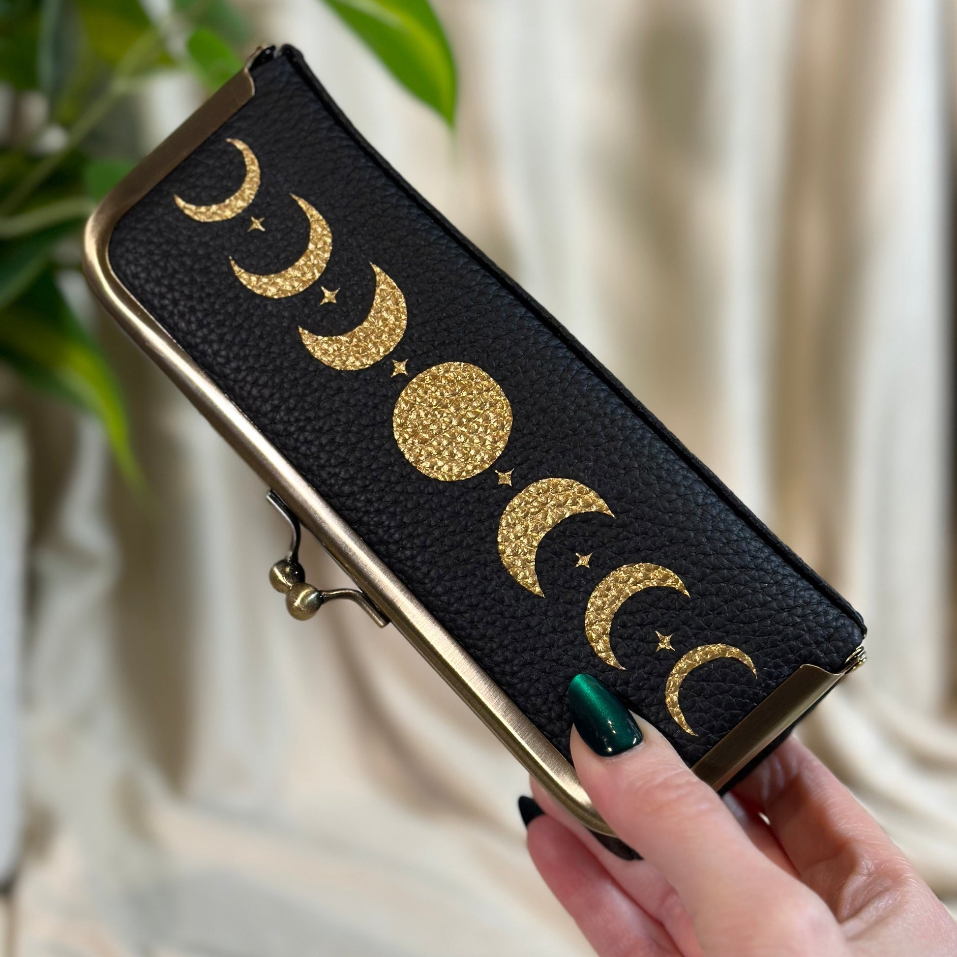 Black wallet with gold moon phases held by a hand against a neutral background