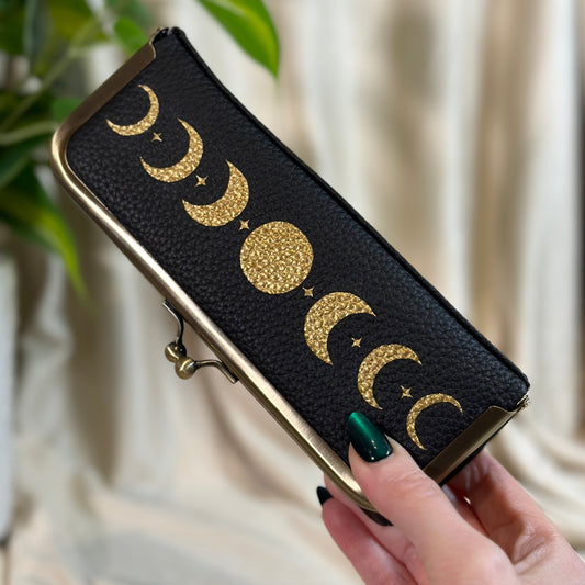 Black wallet with gold moon phases held by a hand against a neutral background