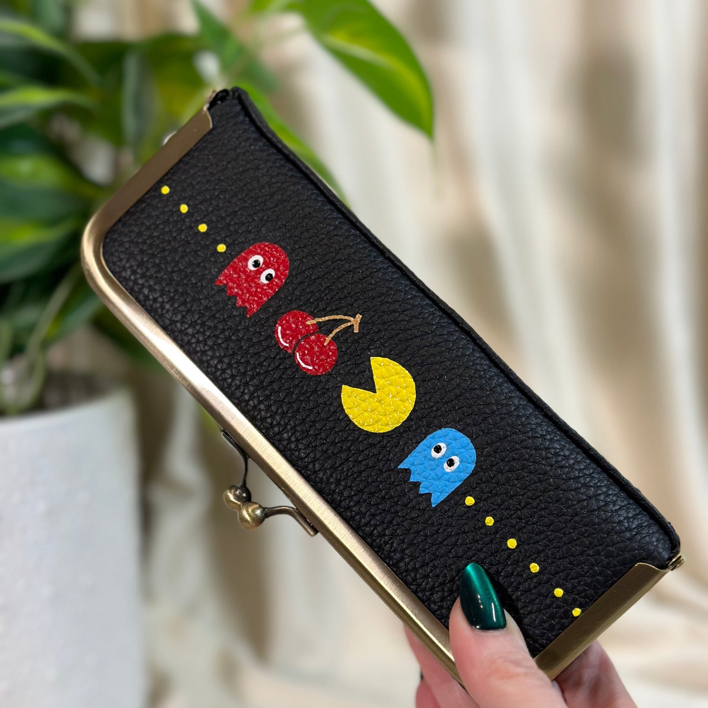 Black wallet with colorful designs held by a hand, with a plant in the background