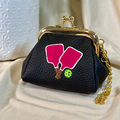 Black purse with pink pickleball paddle design on a beige surface