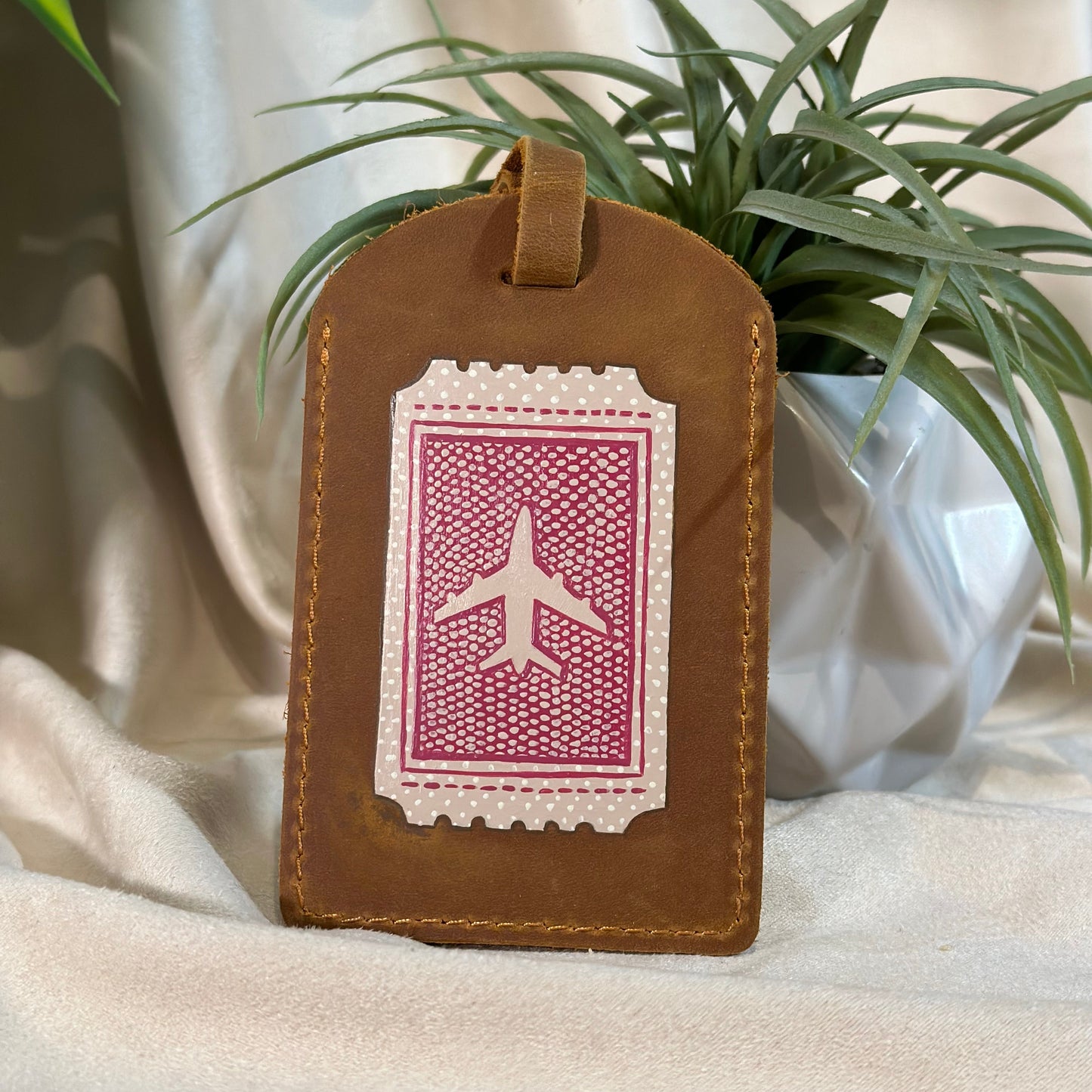 Brown leather luggage tag with airplane design on a white background