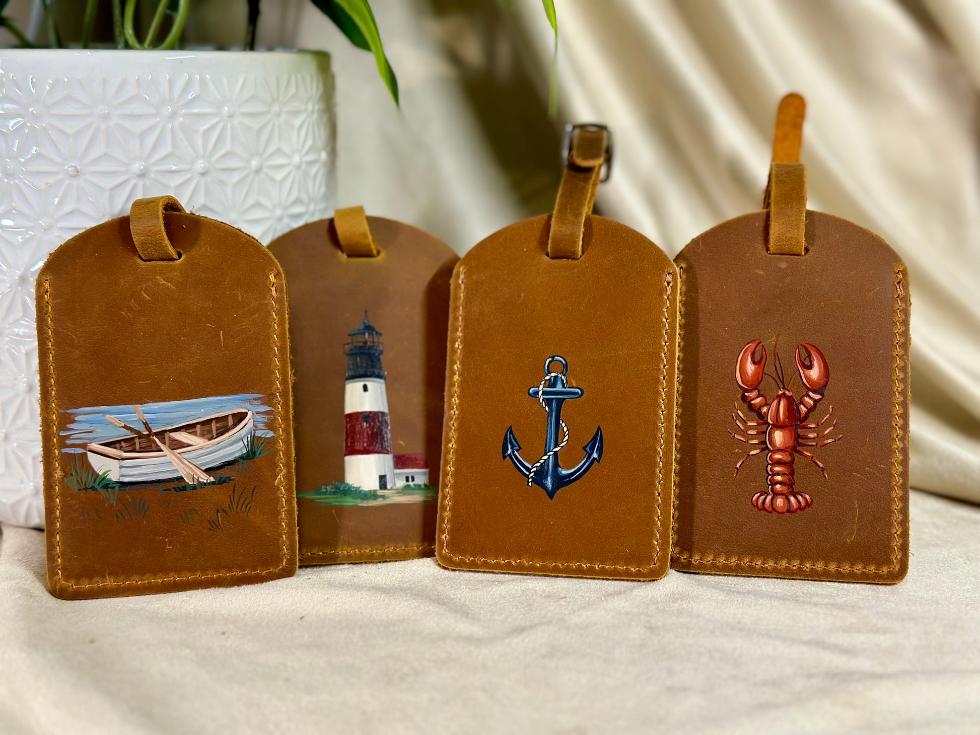 Four brown leather luggage tags with nautical designs on a white surface.