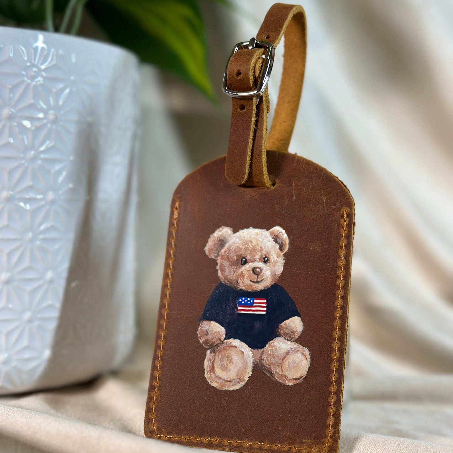 Brown leather luggage tag with teddy bear design on a neutral background