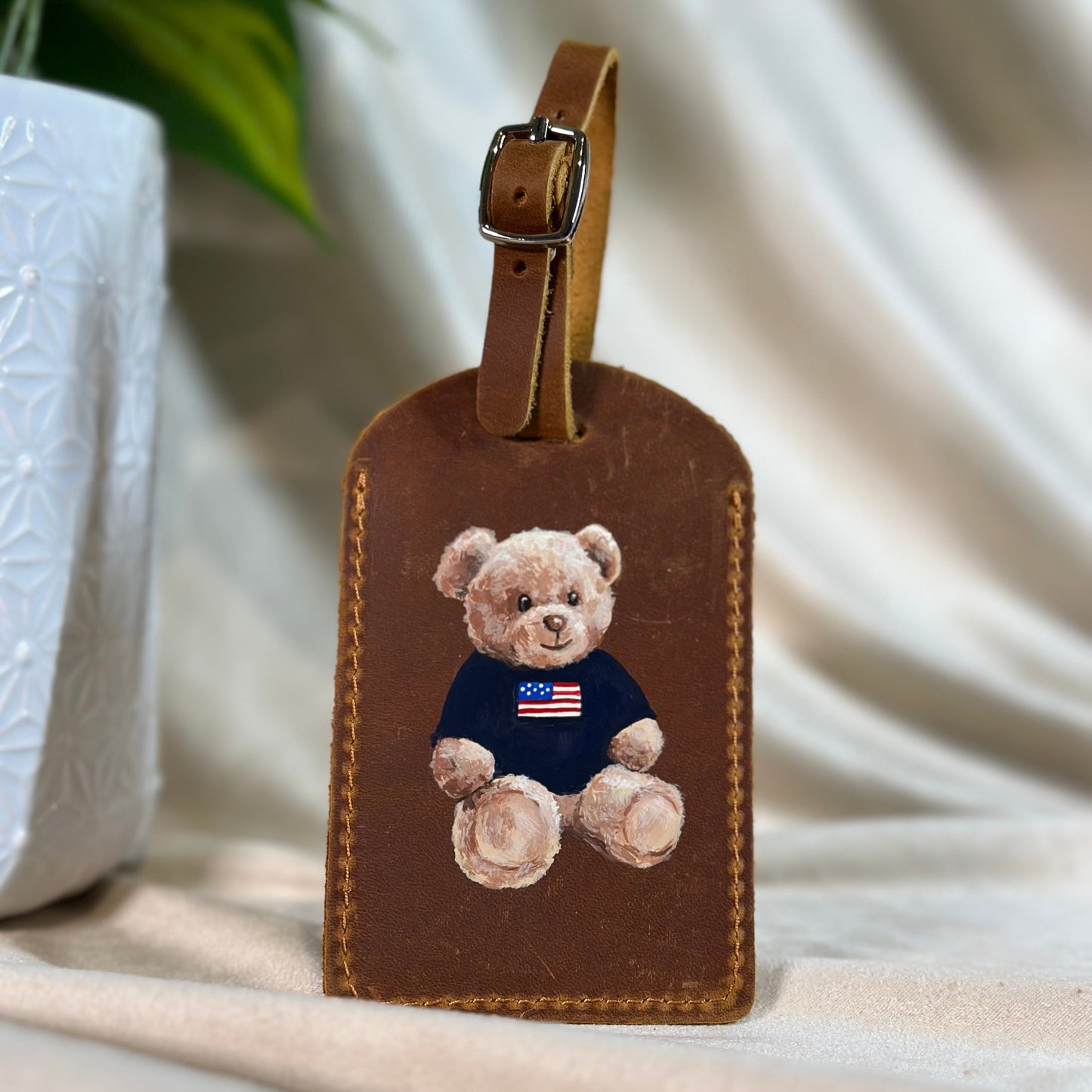 Brown leather luggage tag with a teddy bear design on a white surface.