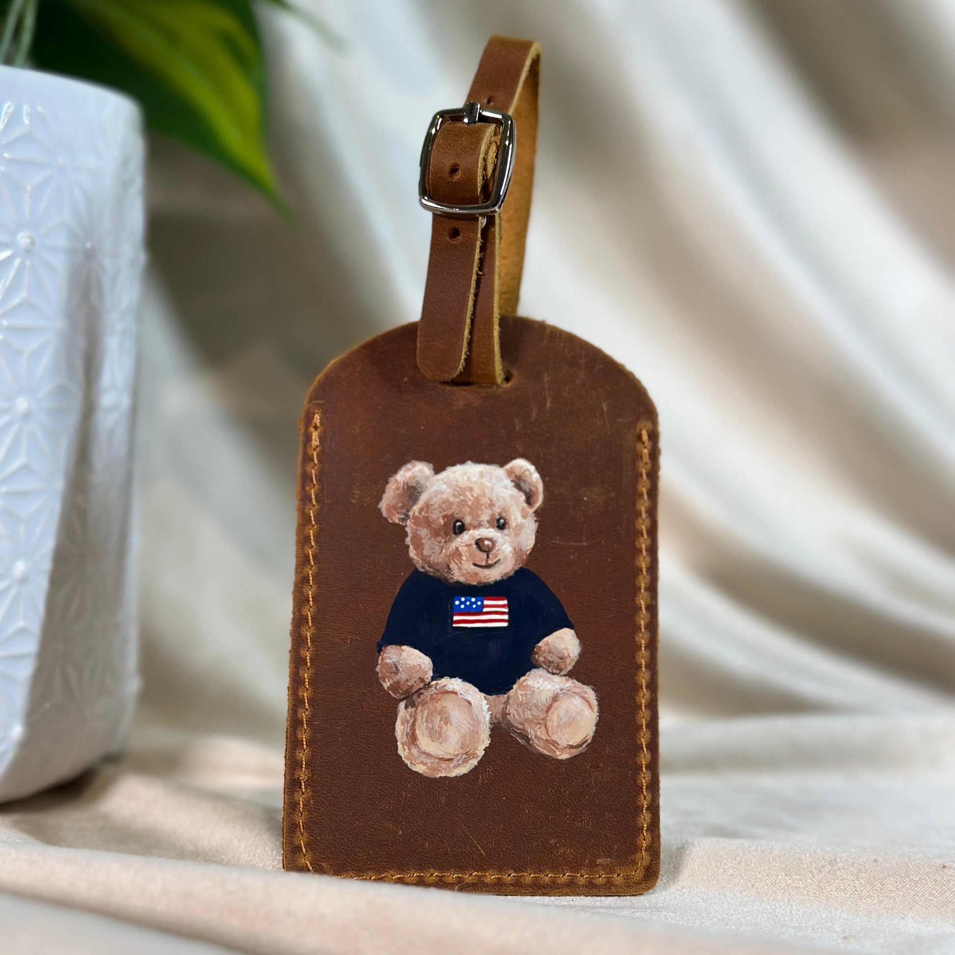 Brown leather luggage tag with a teddy bear design on a white surface.
