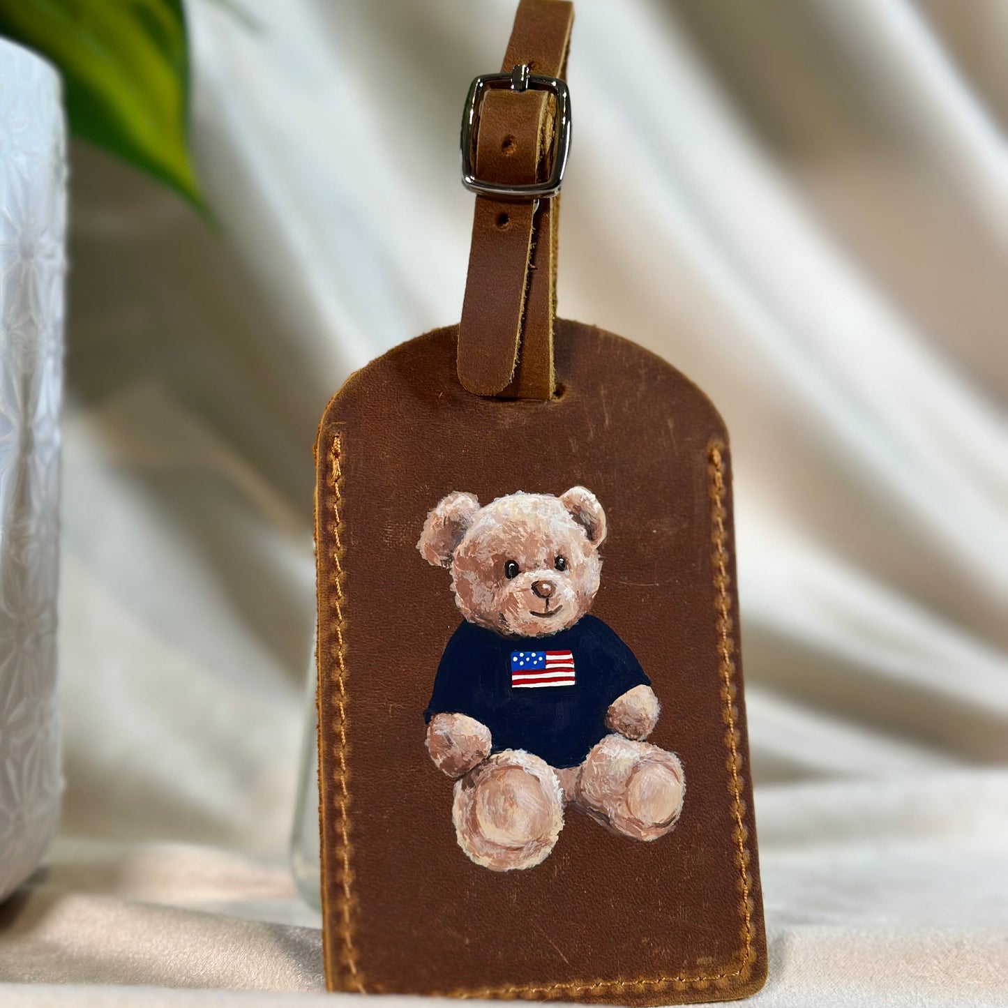 Brown leather luggage tag with a teddy bear design on a soft white background