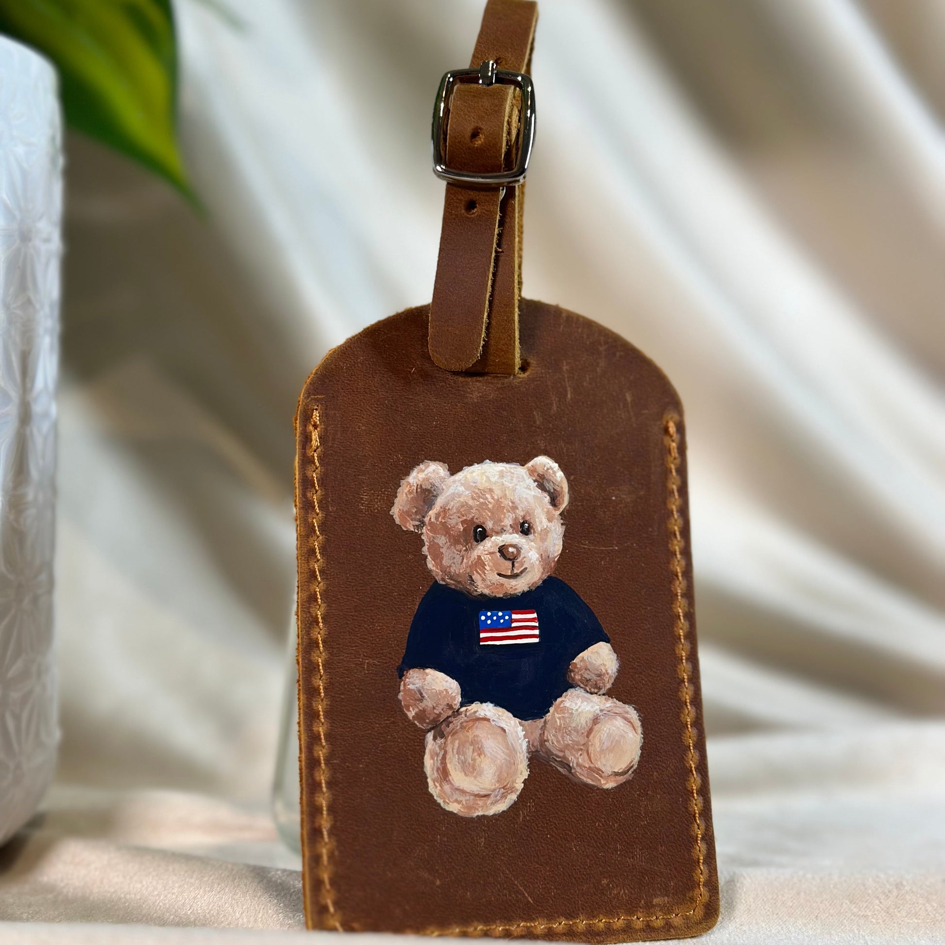 Brown leather luggage tag with a teddy bear design on a soft white background