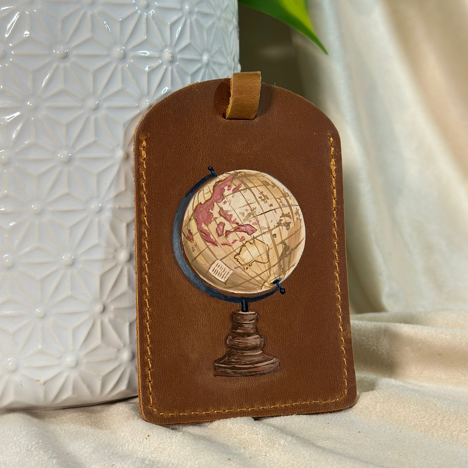 Brown leather luggage tag with globe design on a textured white surface