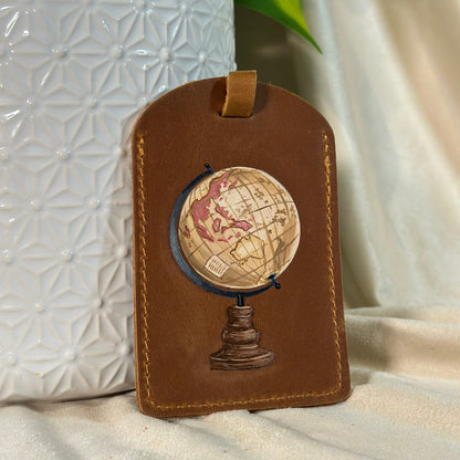 Brown leather luggage tag with globe design on a textured white surface