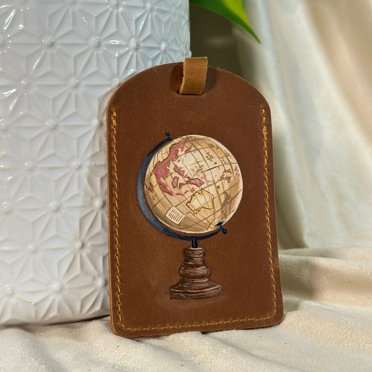 Brown leather luggage tag with globe design on a textured white surface