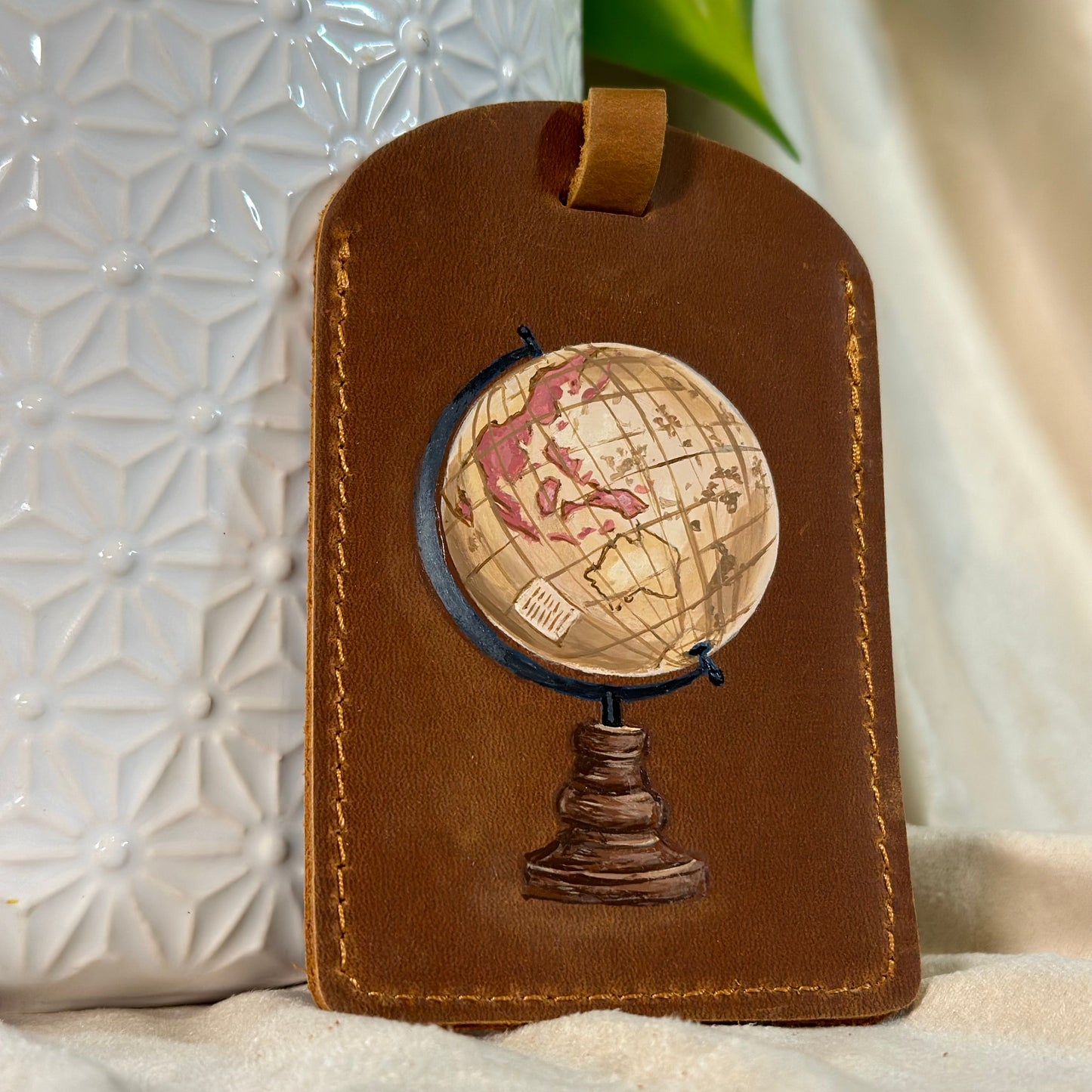 Brown leather luggage tag with a globe design on a white surface