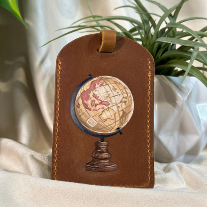 Brown leather luggage tag with embossed globe design on a light fabric background