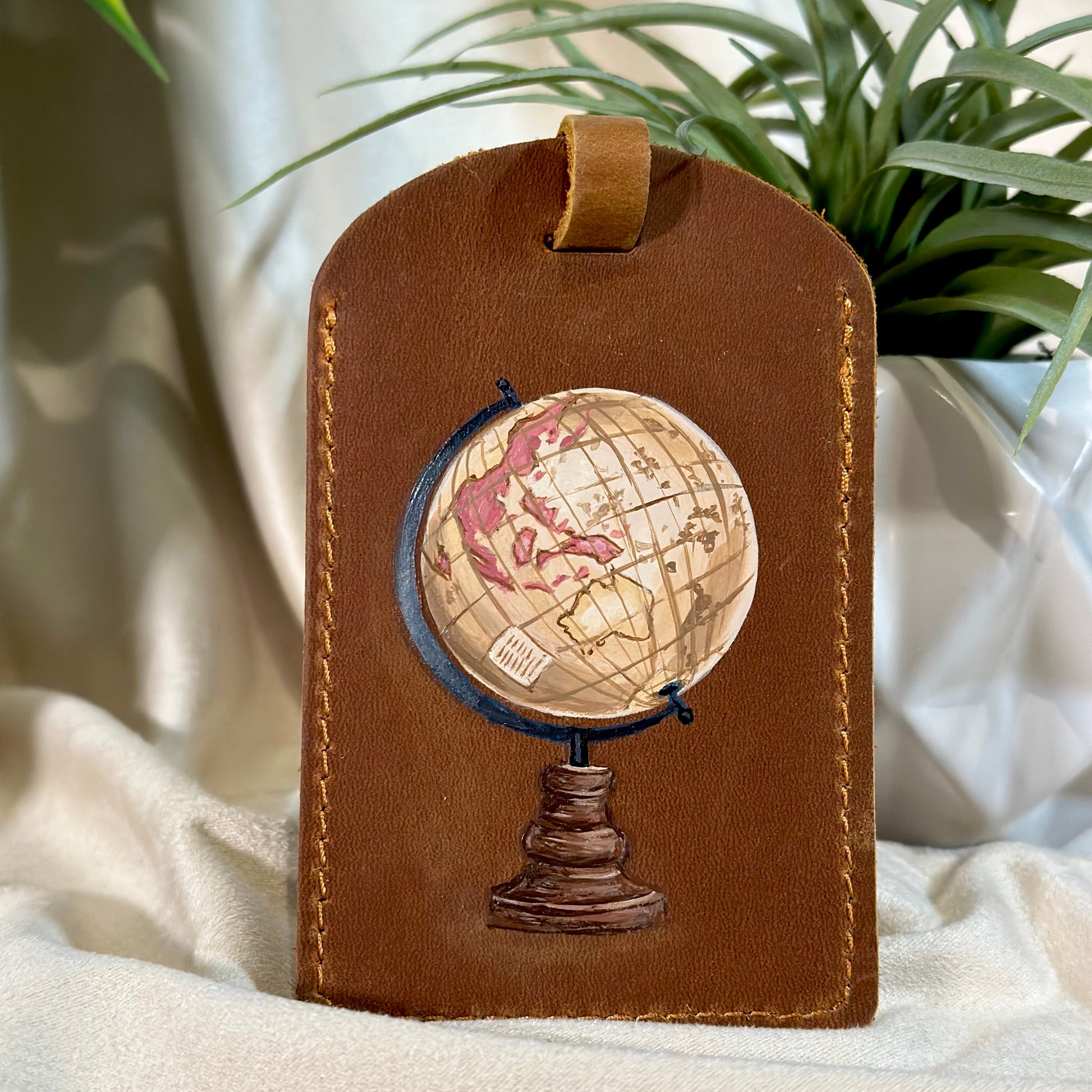 Brown leather luggage tag with globe design on a light fabric background