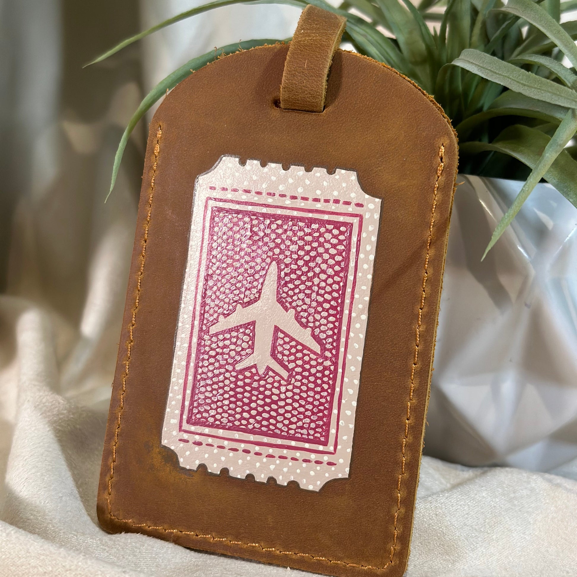 Brown leather luggage tag with airplane design on a light fabric background