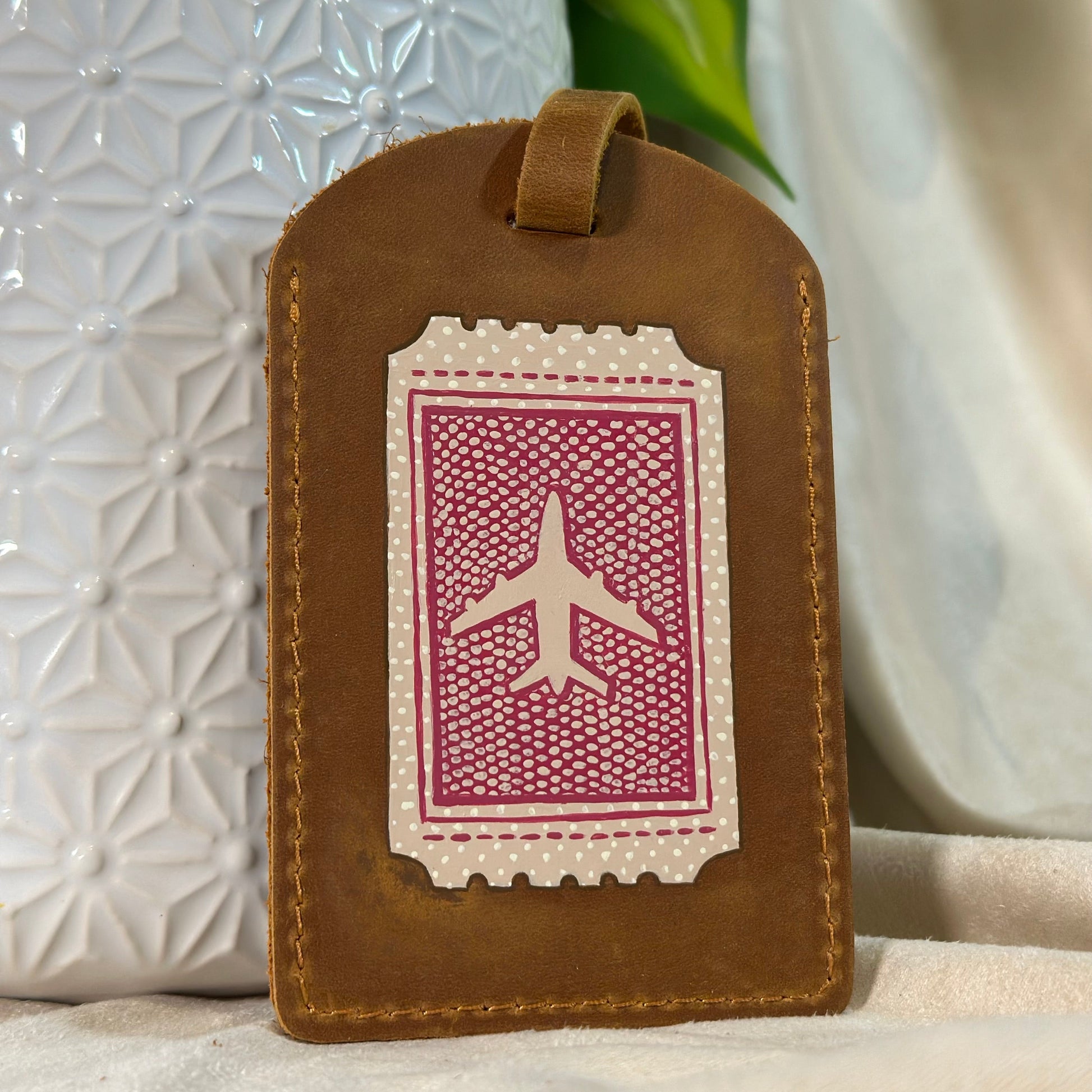 Brown leather luggage tag with airplane design on a neutral background