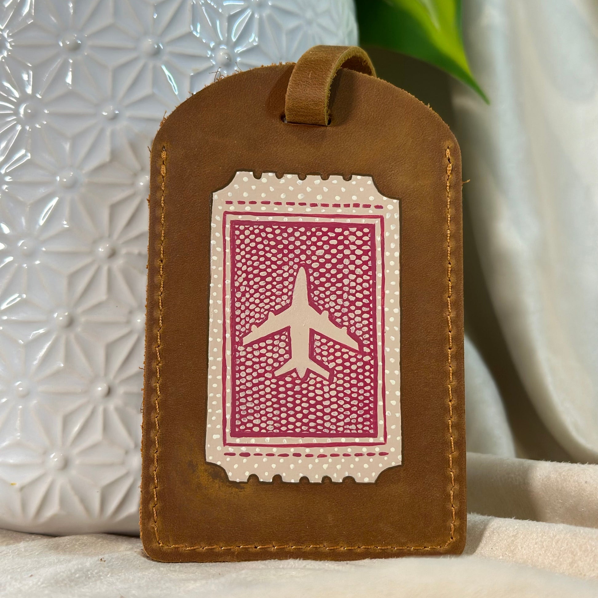 Brown leather luggage tag with airplane design on a neutral background