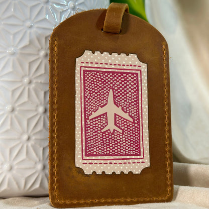 Brown leather luggage tag with airplane design on a textured surface