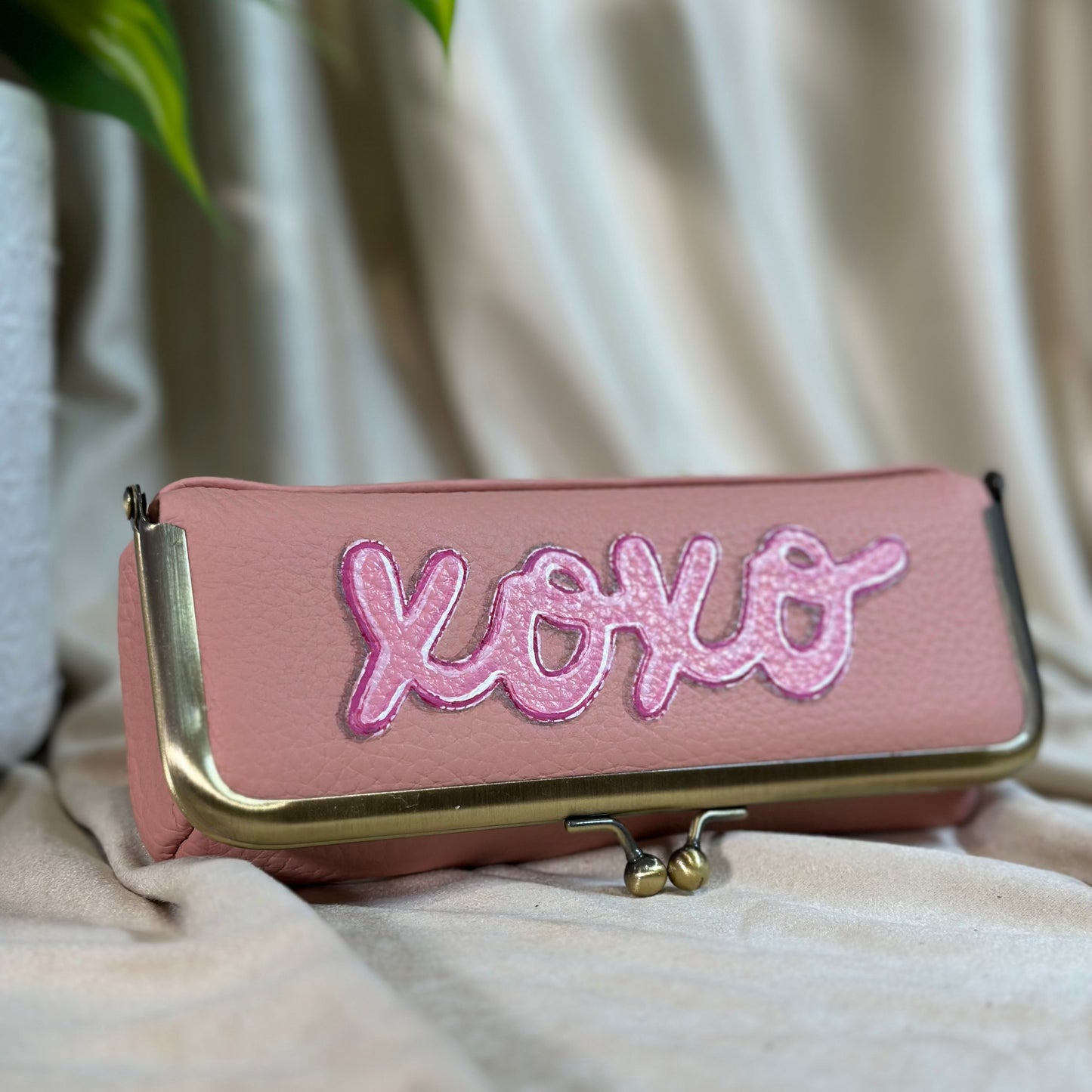 Pink clutch bag with 'XOXO' embroidery on a light fabric background