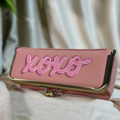 Pink pouch with 'xoxo' embroidery on a beige fabric background