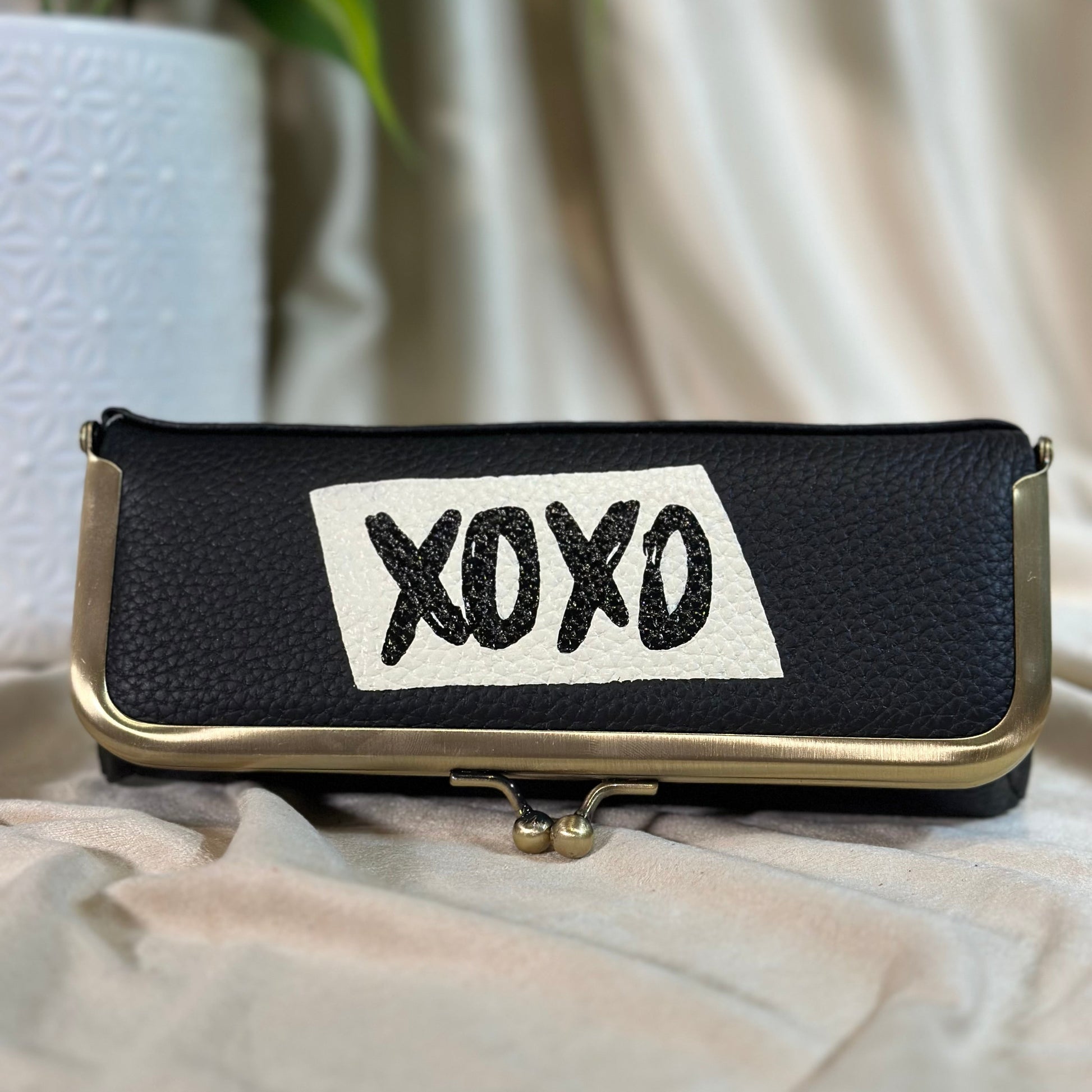 Black pouch with 'XOXO' patch on a light fabric background