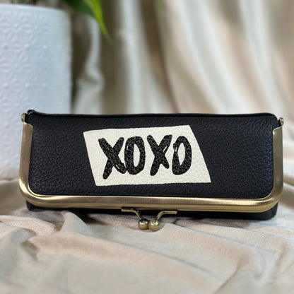 Black pouch with 'XOXO' patch on a light fabric background