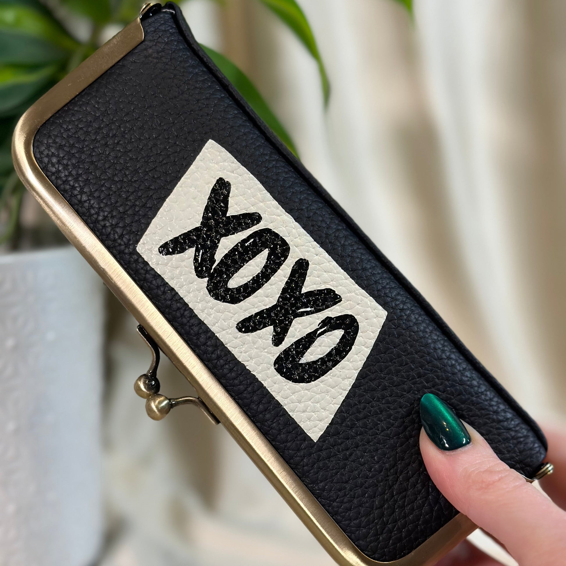 Black pouch with 'XOXO' text held by a hand against a blurred background