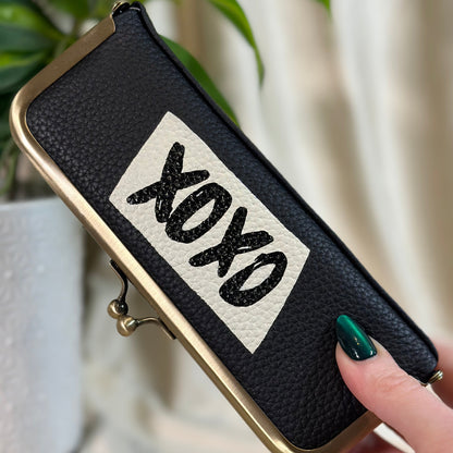 Black pouch with 'XOXO' text held by a hand against a blurred background