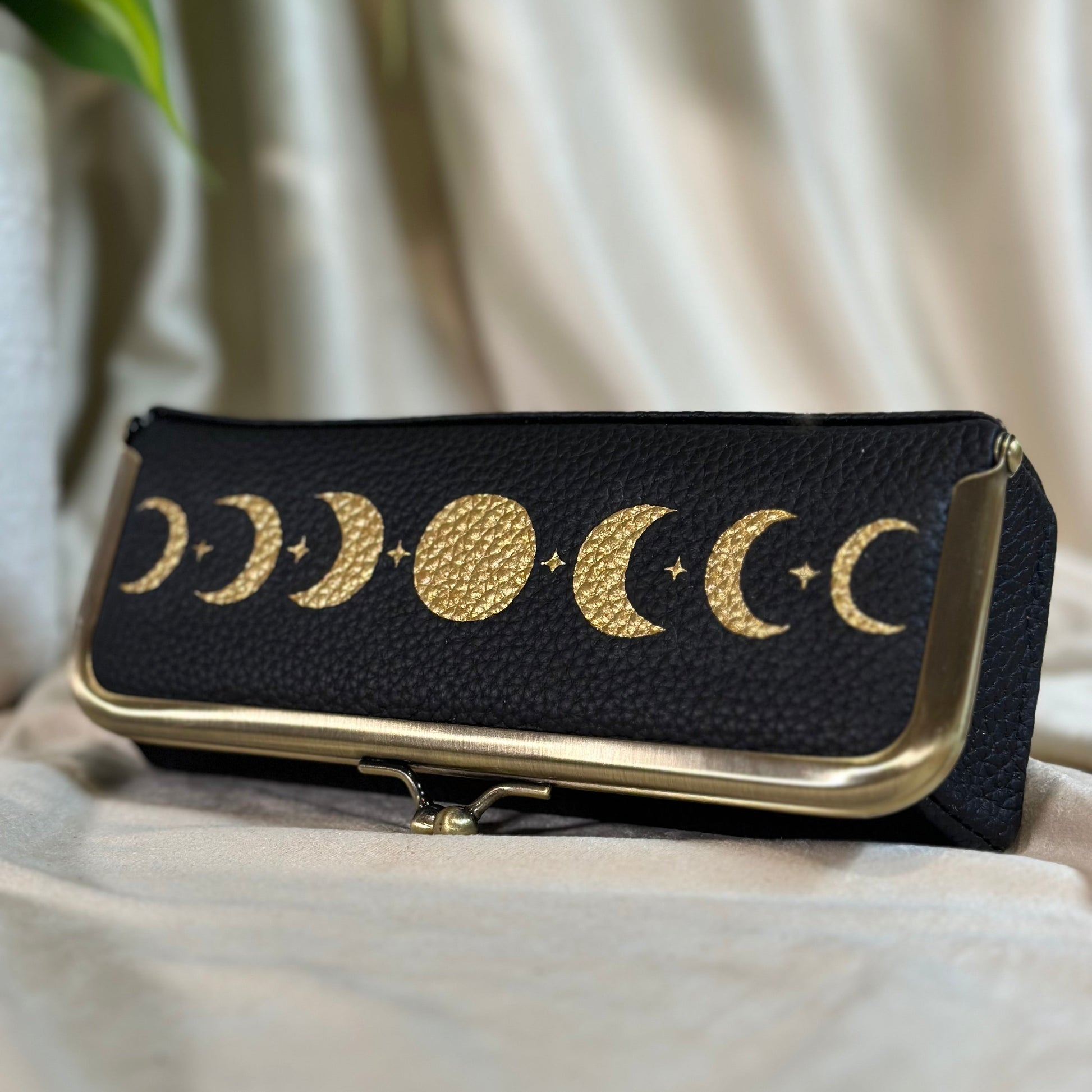 Black pouch with gold moon phases design on a light fabric background