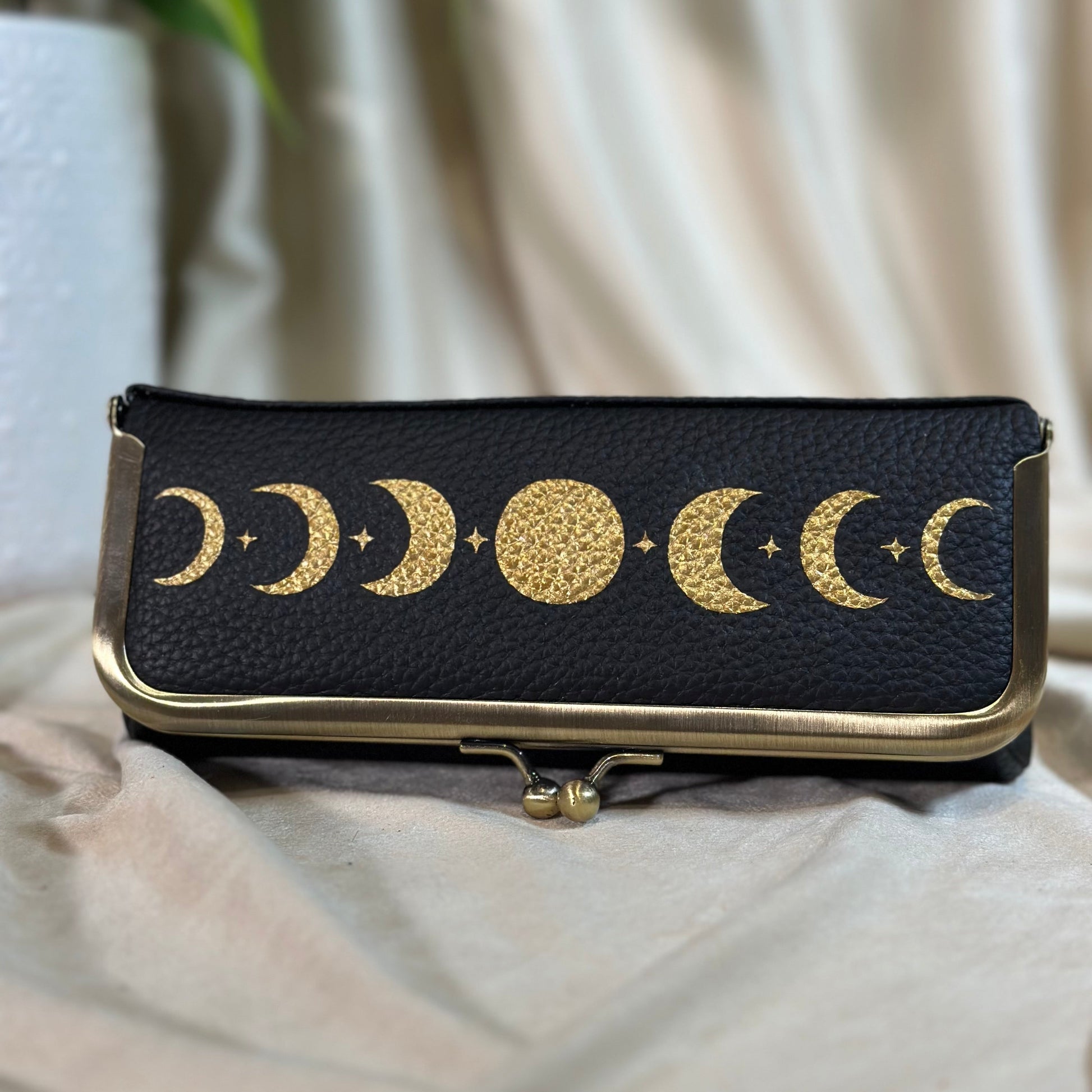 Black pouch with gold moon phases design on a beige fabric background