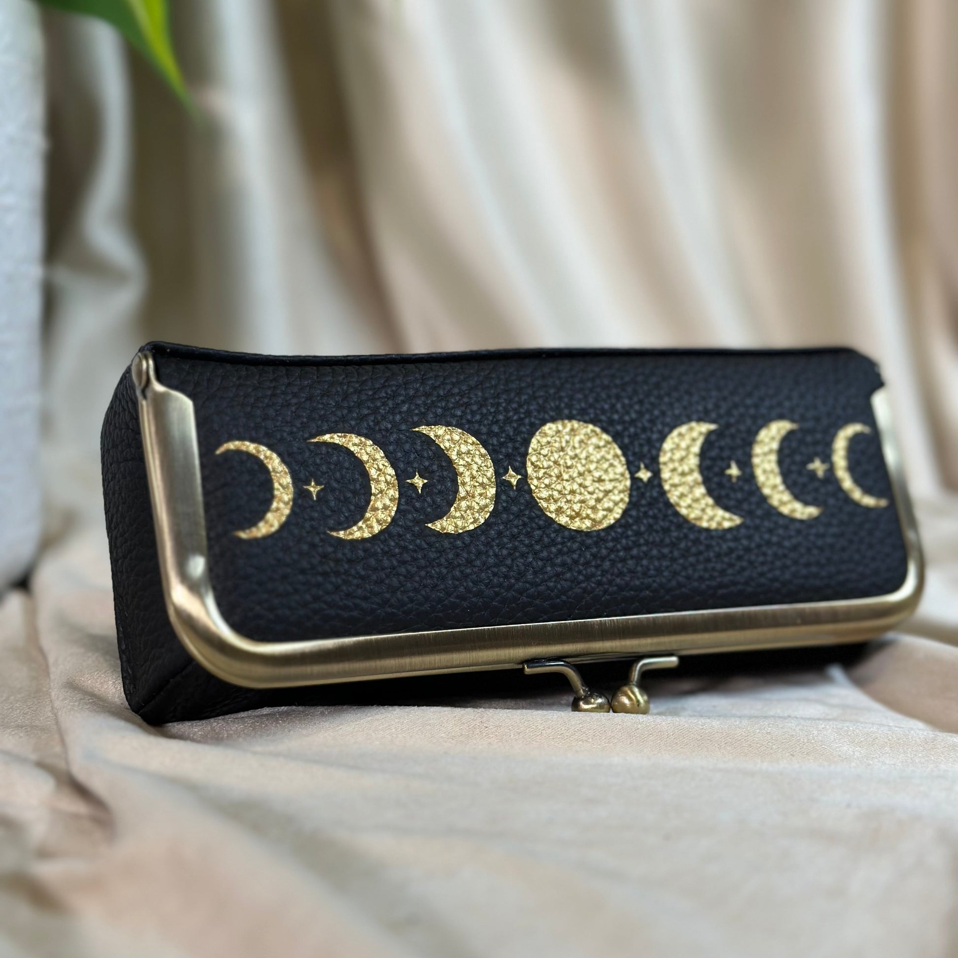 Black clutch with gold moon phases on a light fabric background