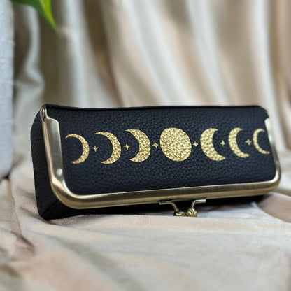 Black clutch with gold moon phases on a light fabric background